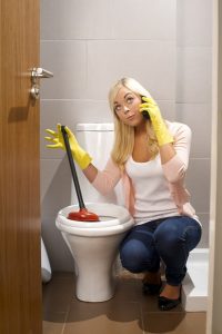 woman with plunger at her toilet, while on the phone