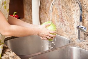 Closeup of the hands of a woman washing a lettuce and some other vegetables in the kitchen sink