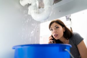 woman-looking-under-sink-at-leaking-pipe-while-on-phone